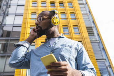 Mann hört Musik über drahtlose Kopfhörer vor einem modernen Gebäude - ASGF01813