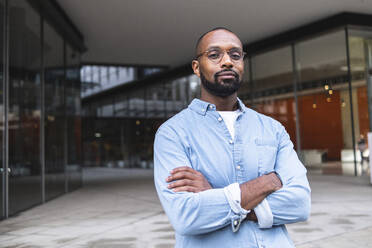 Confident man with arms crossed standing near buildings - ASGF01815