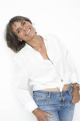 Happy mature woman leaning against white background - JBYF00023