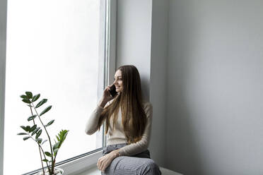 Geschäftsfrau, die mit ihrem Smartphone auf der Fensterbank im Büro sitzt - LLUF00388