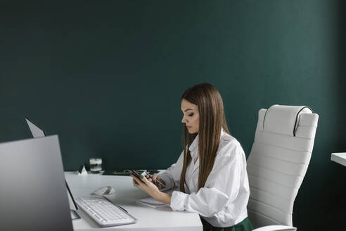 Businesswoman using smart phone at desk in office - LLUF00391