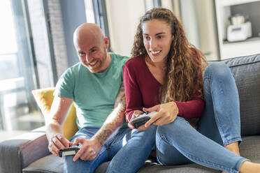 Smiling couple with video game controller playing on sofa - DLTSF02411