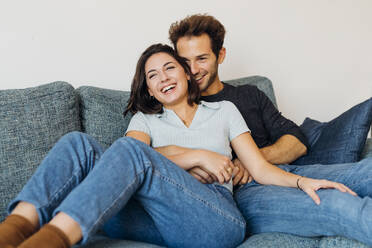 Fröhliches Paar sitzt auf dem Sofa im Wohnzimmer zu Hause - MEUF04716