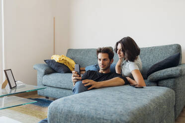 Young couple taking selfie through smart phone in living room at home - MEUF04722