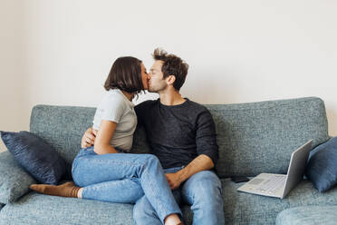 Zärtliches junges Paar küsst sich mit geschlossenen Augen auf dem Sofa zu Hause - MEUF04731