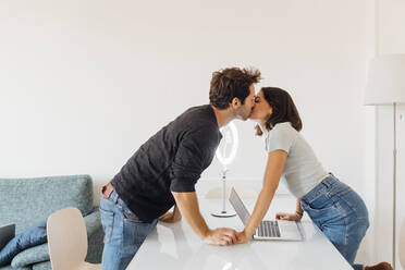 Young couple with laptop on table kissing at home - MEUF04732