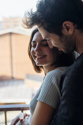 Smiling young couple standing by window at home - MEUF04741