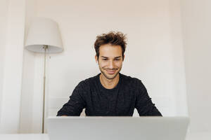 Lächelnder Geschäftsmann bei einem Videogespräch über einen Laptop im Heimbüro - MEUF04748