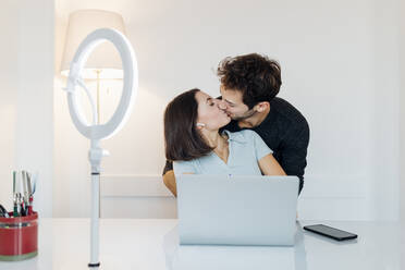 Zärtliches junges Paar mit Laptop, das sich zu Hause küsst - MEUF04758