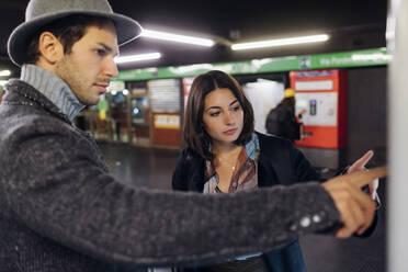 Junger Mann und Frau benutzen Fahrkartenautomat in der U-Bahn-Station - MEUF04762