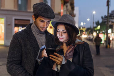 Freundin und Freund benutzen gemeinsam ein Mobiltelefon in der Stadt - MEUF04785