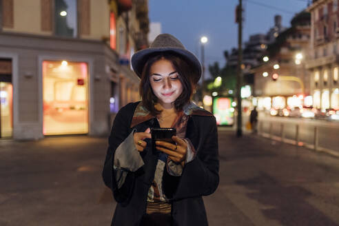 Lächelnde junge Frau, die auf der Straße ein Smartphone benutzt - MEUF04788