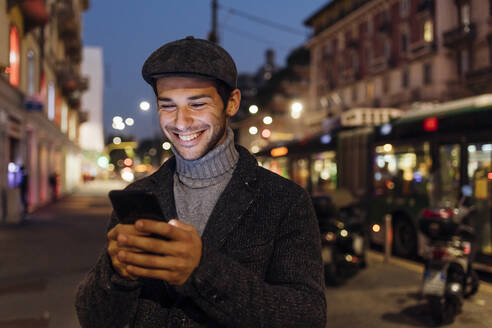 Glücklicher junger Mann, der in der Stadt ein Smartphone benutzt - MEUF04790