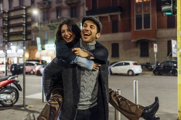 Cheerful boyfriend carrying girlfriend piggyback while walking in city - MEUF04791