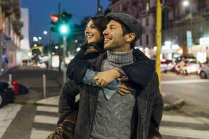 Happy man carrying girlfriend piggyback on city street - MEUF04792