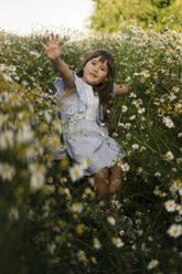 Girl waving amidst flowers in meadow - SSGF00282