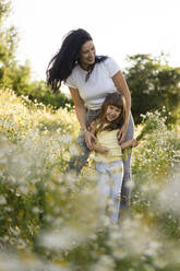 Mother playing with daughter holding bunch of flowers in meadow - SSGF00293