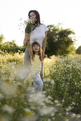 Mother smelling bunch of flowers held by daughter in meadow - SSGF00294