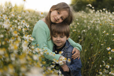 Mädchen mit Arm um Bruder stehend inmitten von Blumen auf einer Wiese - SSGF00298