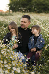 Vater mit Sohn und Tochter kauernd bei Blumen auf einer Wiese - SSGF00300