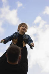 Man holding son aloft under sky - SSGF00301