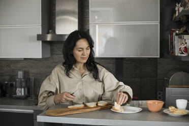 Woman putting butter on bread at table - LLUF00410