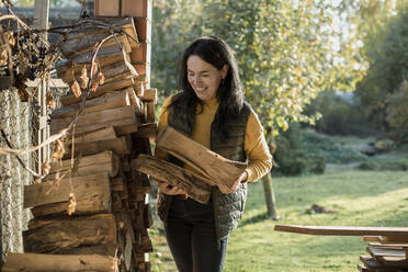 Lächelnde Frau beim Sammeln von Brennholz im Hinterhof - LLUF00416