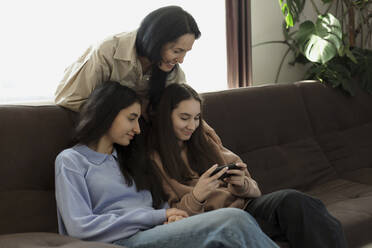 Mutter und Töchter benutzen zu Hause ein Mobiltelefon - LLUF00423