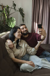 Couple taking selfie through mobile phone on sofa - LLUF00430