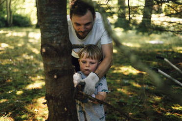 Mann hilft seinem Sohn beim Schneiden eines Astes von einem Baum - ACTF00155