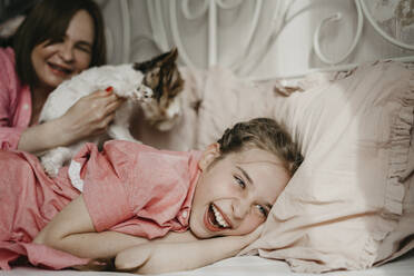 Glückliches Mädchen spielt mit Mutter und Haustier auf dem Bett zu Hause - SEAF00156