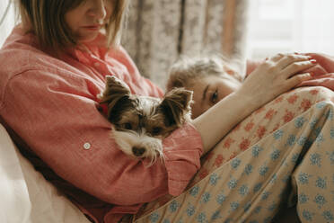 Woman with dog and daughter sitting in bedroom - SEAF00159