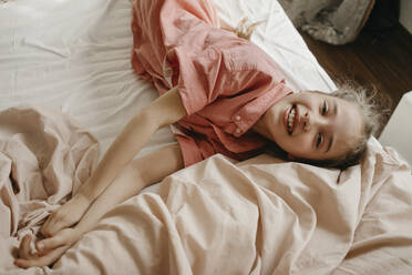 Glückliches Mädchen in Freizeitkleidung auf dem Bett liegend zu Hause - SEAF00167