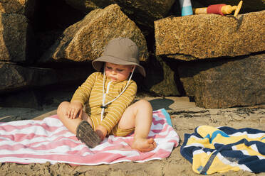 Boy sitting on towel and removing sandal at beach - ACTF00159