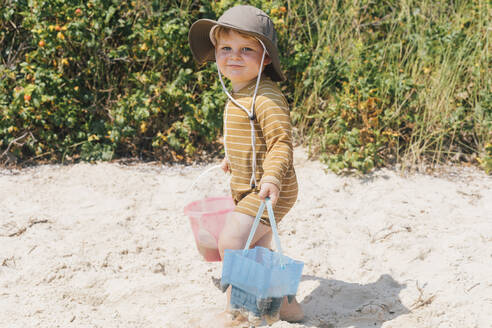 Lächelnd niedlichen Jungen mit Sand Eimer zu Fuß am Strand an einem sonnigen Tag - ACTF00169