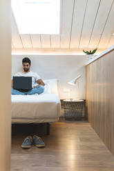 Geschäftsmann benutzt Laptop auf dem Bett im Dachgeschoss seines Hauses - JAQF00932