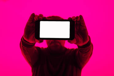 Mann zeigt leeren Bildschirm des Smartphones vor rosa Hintergrund - GPF00232