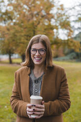 Frau mit Einweg-Kaffeebecher lachend im Park - MGIF01120