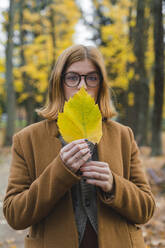 Frau hält Herbstblatt vor dem Mund im Park - MGIF01121