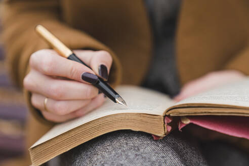 Frau mit Füllfederhalter schreibt in einem Buch im Park - MGIF01124