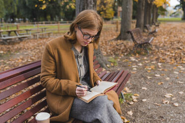 Young woman writing in book in public park - MGIF01126