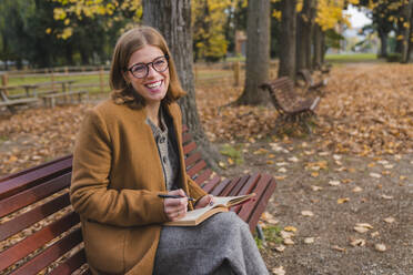 Woman with book laughing on park bench - MGIF01127