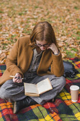 Young woman reading book in autumn park - MGIF01137