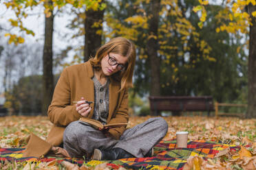 Woman with pen reading book in autumn park - MGIF01138