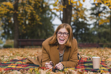 Woman lying on blanket and laughing at autumn park - MGIF01141