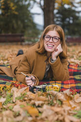 Glückliche Frau auf einer Decke liegend im herbstlichen Park - MGIF01142