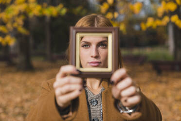 Junge Frau schaut durch einen Fotorahmen im herbstlichen Park - MGIF01148