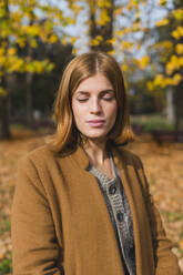 Young woman with eyes closed standing in autumn park - MGIF01150