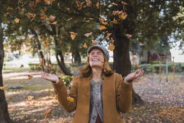 Cheerful woman throwing autumn leaves in air - MGIF01160
