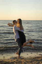 Playful man picking up woman at water's edge - SSGF00321